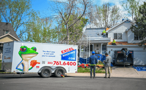 Excel Roofing crew doing a full roof replacement on a multistory home with an Excel Roofing bathroom trailer out front