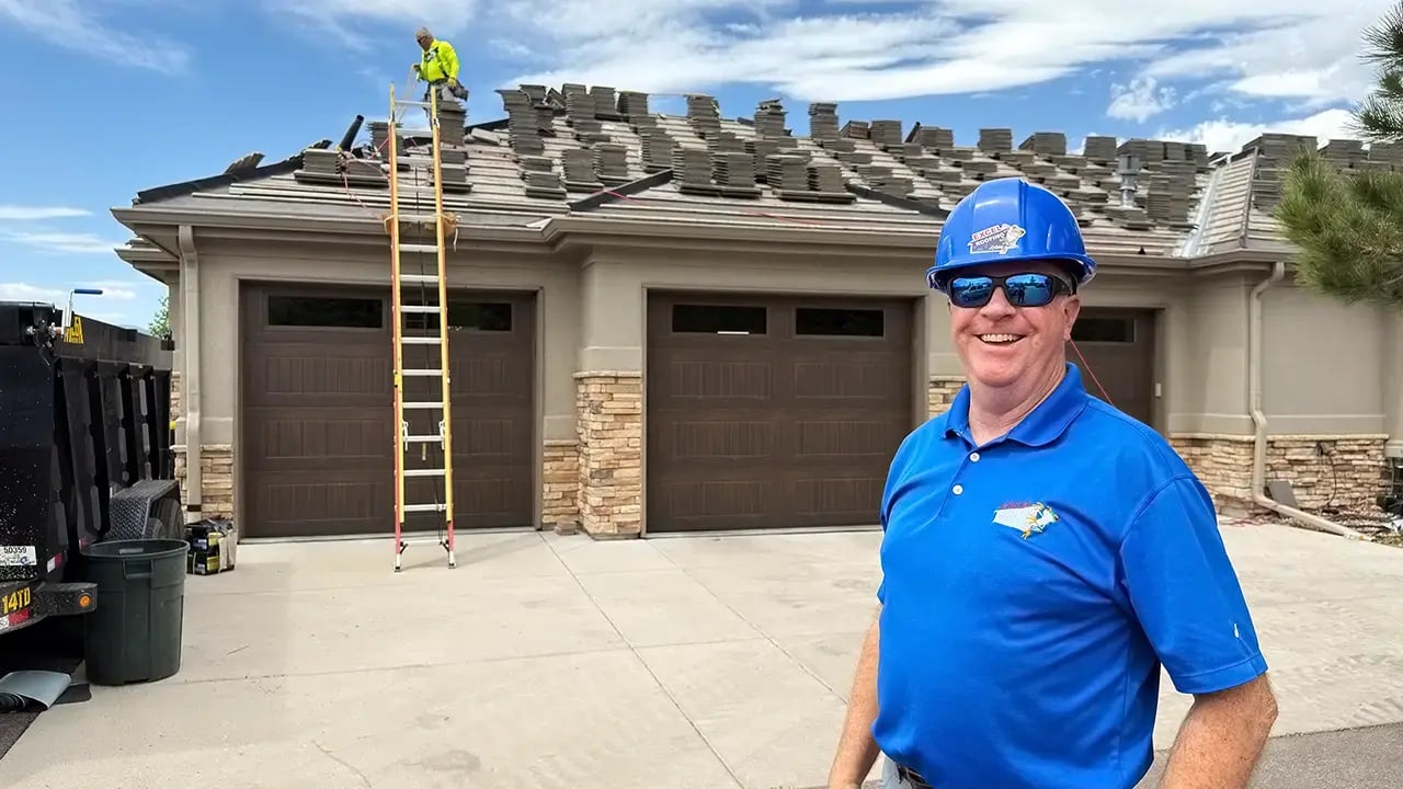 Excel Roofing Senior Project Manager Kevin McCarthy wearing a blue hard hat and blue polo shirt in front of a large home recieving a new concrete tile roof