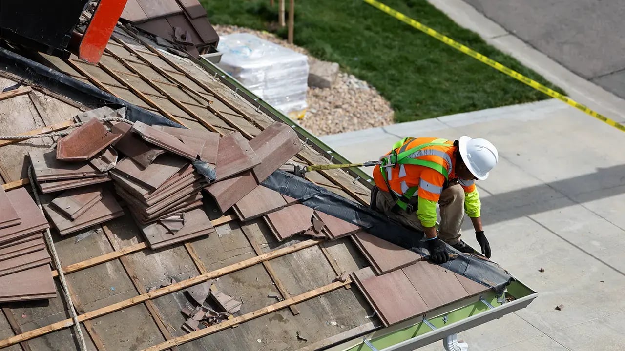 Excel Roofing contractor in full safety gear and hard hat, removing concrete tile from a townhome_1