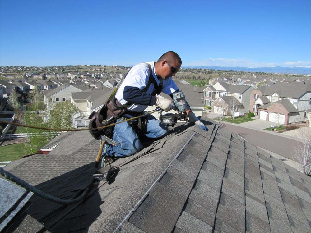 Excel Roofing Contractor, wearing safety gear and tied off to the roof, nailing ridge shingles into place