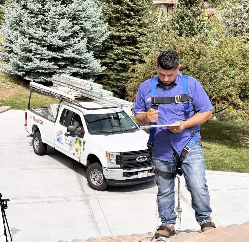 Excel Roofing Project Manager in blue shirt, inspecting a roof and writing down what he sees