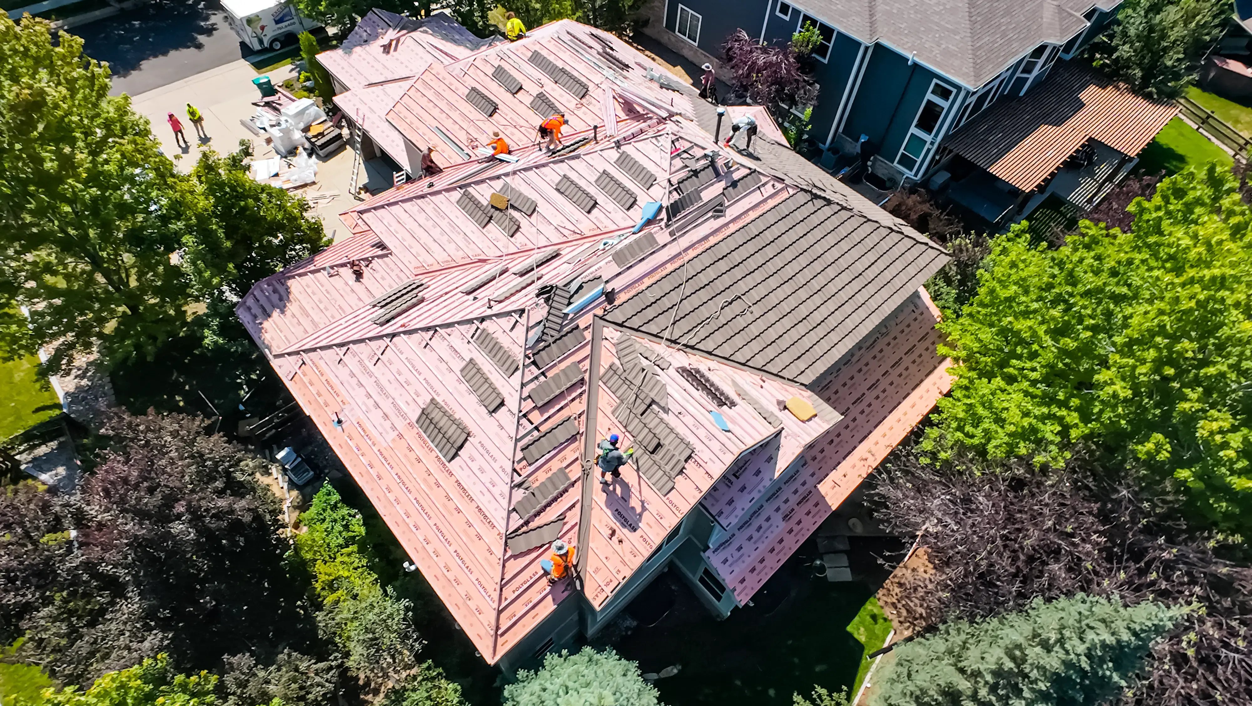 a multi-story colorado home with a stone coated steel roof being installed. On top of the pink underlayment are many wooden battens that the steel panels are being installed on top of