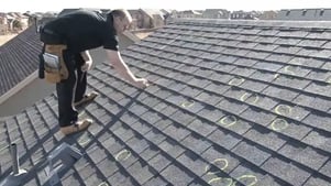 Experienced roofer circles hail damage with chalk on an asphalt shingle roof.