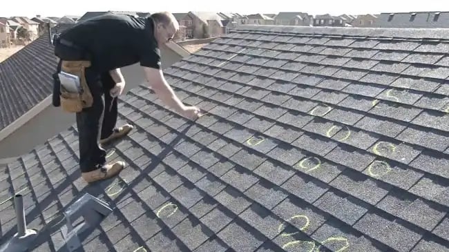 Experienced roofer circles hail damage with chalk on an asphalt shingle roof.
