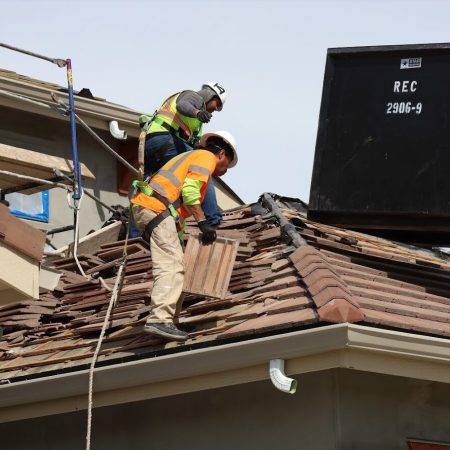 Man with a hard hat and harness standing on roof, inspecting the work he has done.